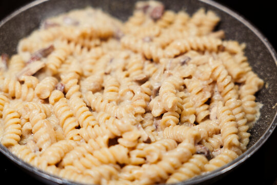 Fusilli pasta cooking in creamy mushroom sauce in pan. Close up of creamy fusilli dish with mushroom sauce.