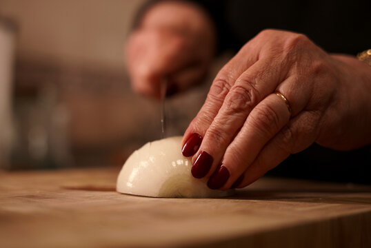 Slicing onion with knife on wooden cutting board close-up. Woman cutting fresh onion in thin slices.