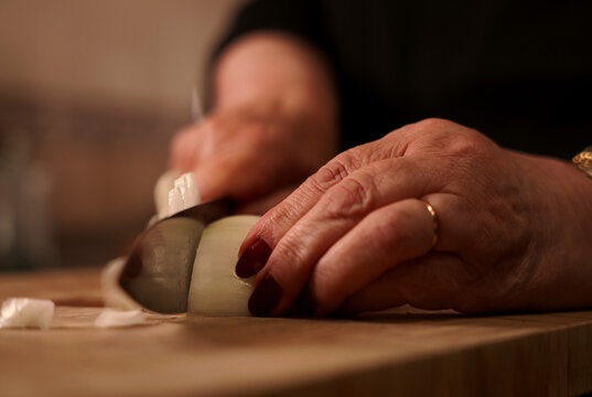 Julienne cutting onion with knife on wooden cutting board. Woman chopping fresh onion with knife.