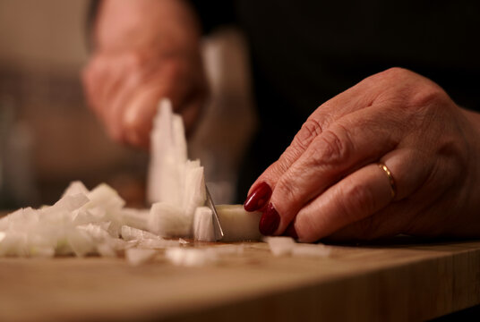 Dicing onion with knife on wooden cutting board close-up. Woman chopping fresh onion in dice with knife.