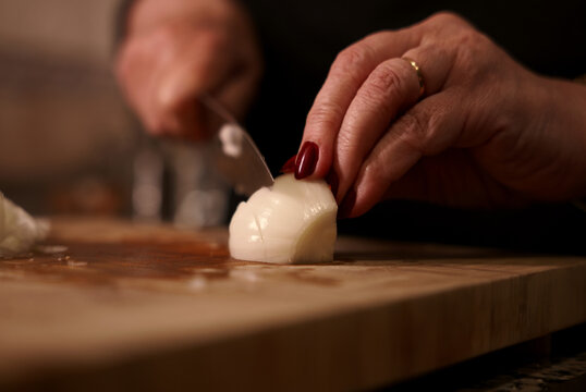 Julienne cutting onion with knife on wooden cutting board. Woman chopping fresh onion with knife.