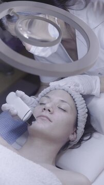 Relaxed woman receives gentle facial cleansing under soft ring light