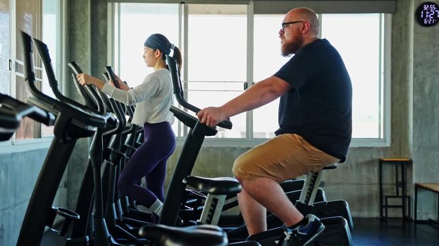 Diverse group engaging in indoor cycling workout at modern gym with fitness equipment and natural light