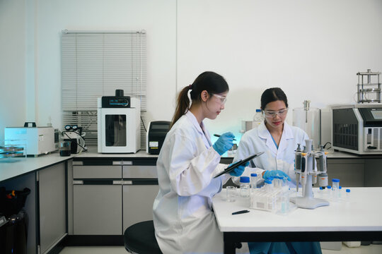 Two Asian Female Scientists Working Together in Modern Research Laboratory with Equipment and Samples