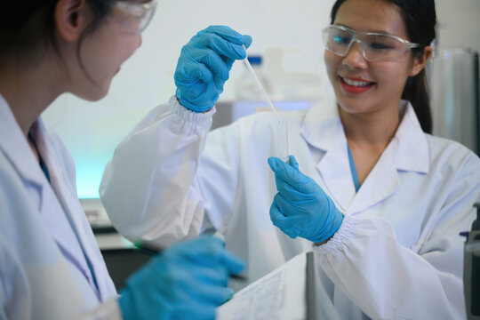 Two Female Scientists Examining Sample in Test Tube in Modern Laboratory