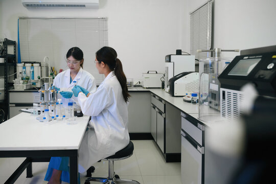 Two Female Asian Scientists Working Together in Modern Laboratory with Test Tubes and Scientific Equipment
