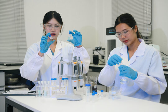 Two Asian Female Scientists Working Together in Modern Laboratory with Test Tubes and Lab Equipment