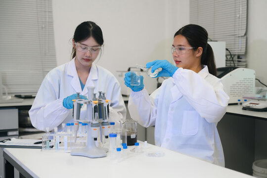 Two Young Asian Female Scientists Conducting Experiments in Modern Laboratory with Beakers and Pipettes
