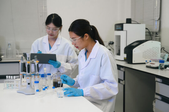 Two Asian Female Scientists Working Together in Modern Laboratory with Pipettes and Lab Equipment