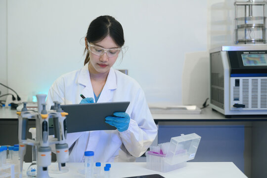 Young Asian Female Scientist Writing Notes on Clipboard in Modern Research Laboratory