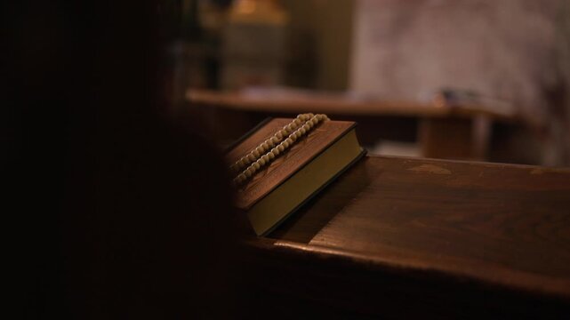 Catholic Bible and rosary with cross resting on a wooden church pew, symbolizing Christian faith, prayer and devotion.