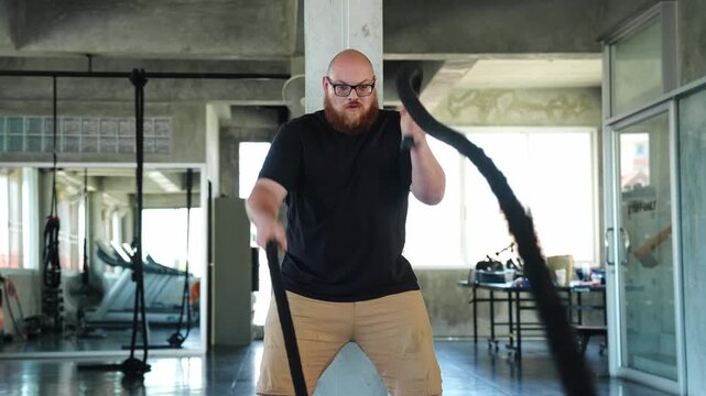 Athletic man engaging in intense battle rope workout in a modern gym setting showcasing strength and determination