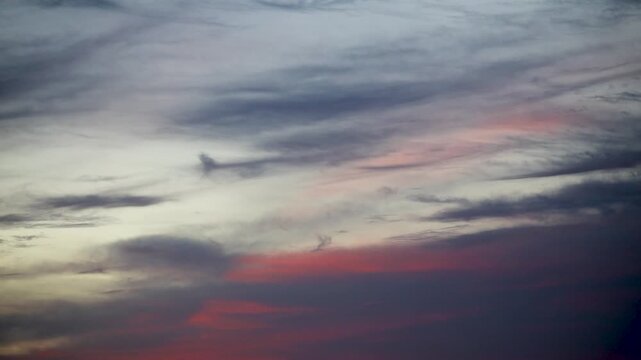 Airplane flies through a cloudy sky during sunset twilight.