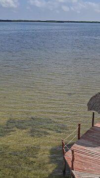 Scenic tropical lagoon surrounded by mangrove forest in Rio Lagartos, Yucatan, Mexico, with traditional thatched palapas and wooden pier under a dramatic cloudy blue sky. Peaceful ecotourism destinati