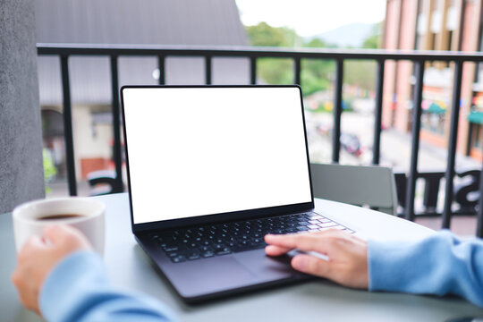 Mockup image of a woman working on laptop computer with blank white desktop screen while drinking coffee in cafe