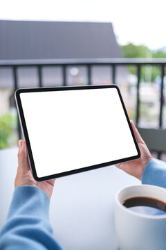 Vertical mockup image of a woman holding digital tablet with blank white desktop screen in cafe