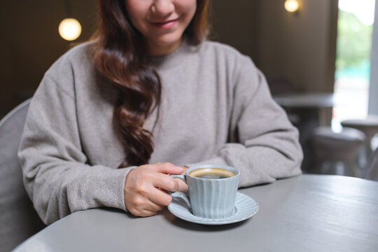Closeup image of a woman holding and drinking hot coffee in cafe