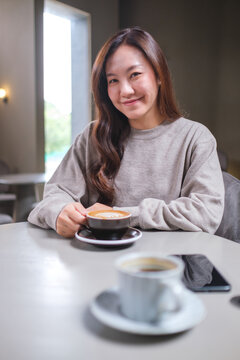 Portrait image of a woman holding and drinking coffee with friend in cafe