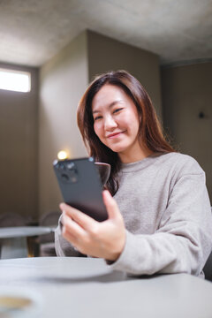 Vertical portrait image of a woman drinking coffee while using mobile phone in cafe