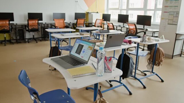 Empty modern classroom displaying laptops, notebooks, and water bottles on desks. Footage serves as ideal background for educational technology promos or school marketing campaigns