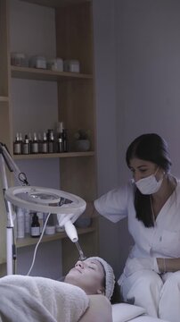 Masked therapist leans in for detailed facial care under warm light