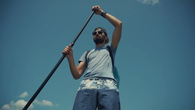 Stand Up Paddleboarder Holding Oar While Rowing On Water Under Blue Sky 