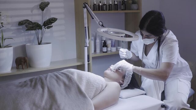 Skincare professional cleansing client face under magnifying lamp