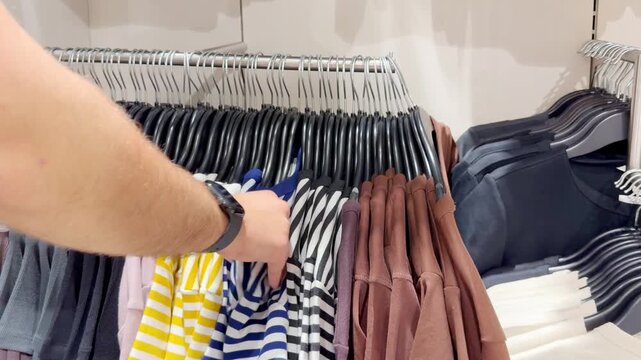 Assorted Casual Clothes on Store Racks.Hand Choosing Clothes on Hangers in Clothing Boutique &ndash; Casual Wear Selection