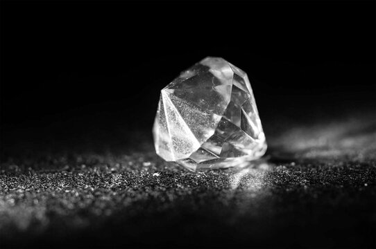 Large faceted diamond crystal placed on dark reflective surface macro shot