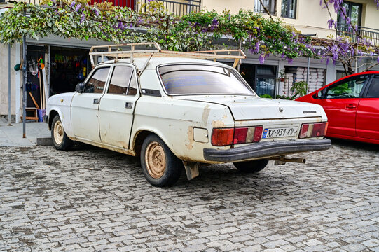 A white GAZ-24 Volga sedan vintage car with a roof rack is parked on cobblestones in front of a store in Kutaisi; a Soviet classic sedan from the 1980s, Imereti region, Georgia 5.4.25