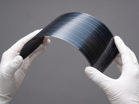 柔軟に曲がるフィルム型太陽電池を両手で持つ様子、日本産ペロブスカイト太陽電池の技術力 / Hands holding and bending a flexible film-type solar panel, showcasing made-in-Japan perovskite solar cell technology