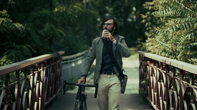 Businessman Walking With Bicycle On Bridge Holding Coffee Cup In City Park 