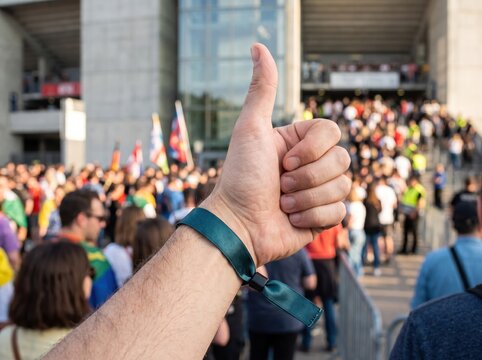 Thumbs Up at the Event Entrance: A close-up shot captures a hand giving a thumbs-up gesture in front of a bustling event entrance.