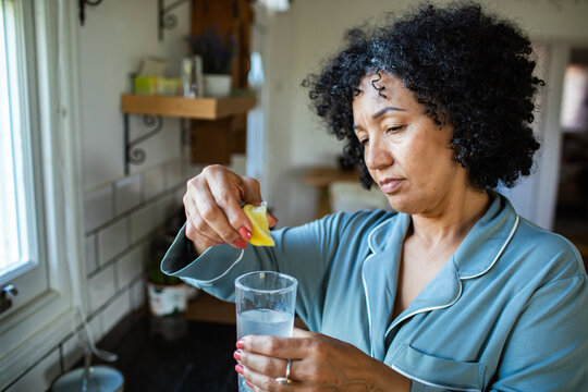 Middle-aged woman squeezing lemon into water at home kitchen