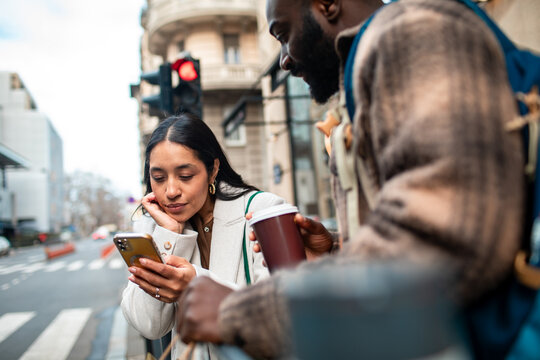 Friends checking smartphone while waiting at city crosswalk