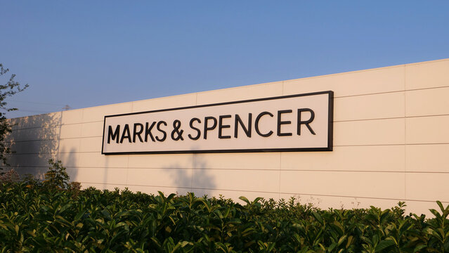 Leicester, England, UK - 17 July 2026: Marks and Spencer retail store sign on white wall facade above green hedge against clear sky