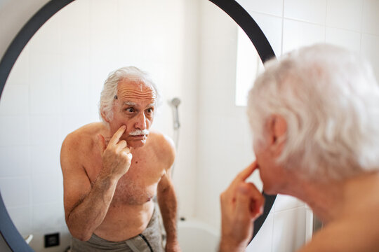 Senior man checking wrinkles in bathroom mirror