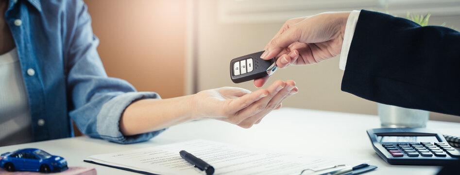 Car rental service concept. Close up view Hand of agent giving car key to customer after signed rental contract form.