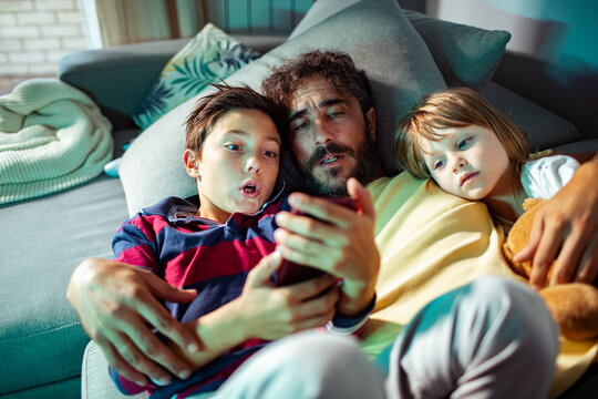 Father with son and daughter watching smartphone on couch at home