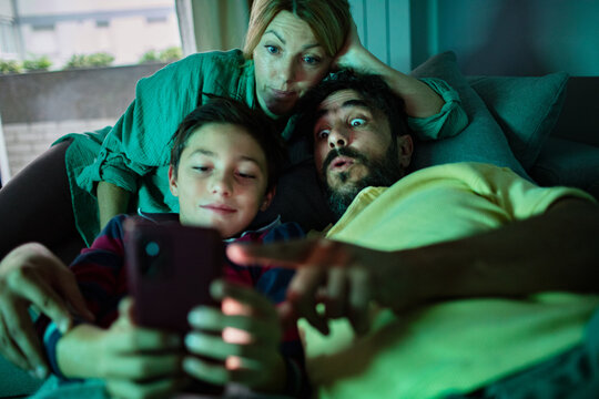 Parents and son watching smartphone on couch at home