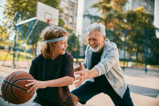 Senior man coaching boy playing basketball on outdoor court