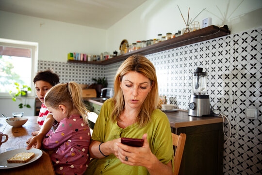 Mother checking smartphone at breakfast table with kids at home