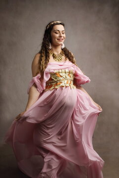 Smiling Pregnant Woman as Ancient Greek Goddess in Pink Toga