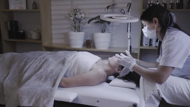 Gloved hands gently massaging client forehead in calming facial routine