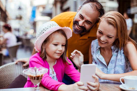 Parents with daughter using smartphone at outdoor cafe