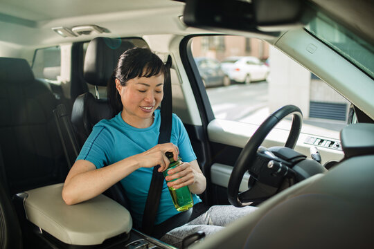 Smiling woman driver opening water bottle inside car on urban street