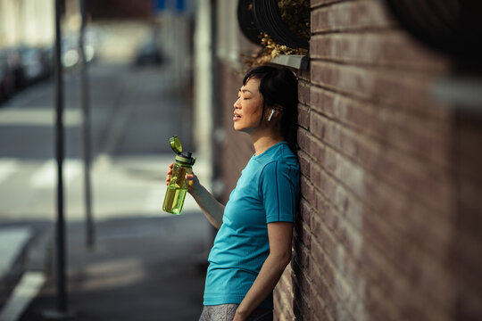 Woman runner hydrating against a brick wall on a city street