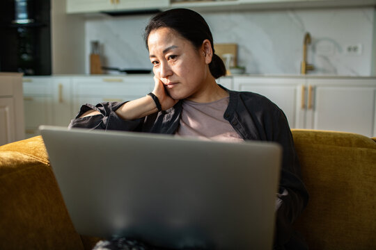 Thoughtful woman using laptop on sofa at home