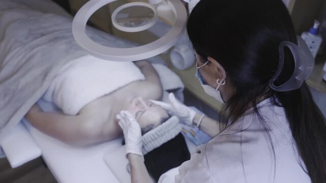 Attentive esthetician performing calming facial massage under ring light