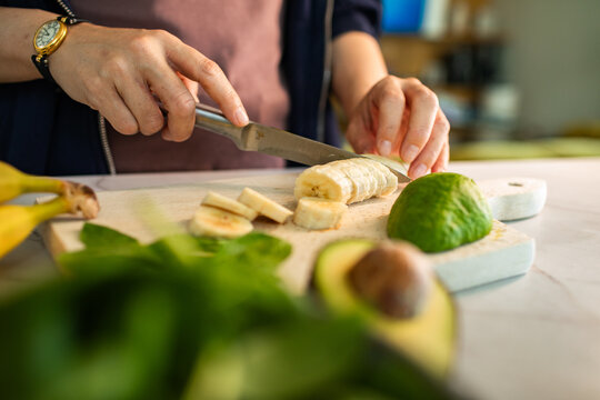 Person slicing banana on cutting board in home kitchen